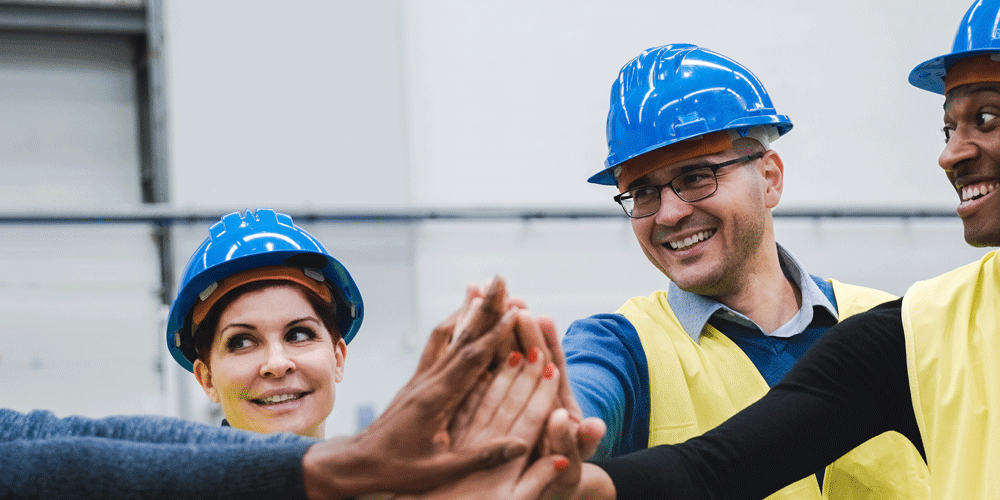 Engineers in blue hard hats and bright yellow vests high-fiving one another.